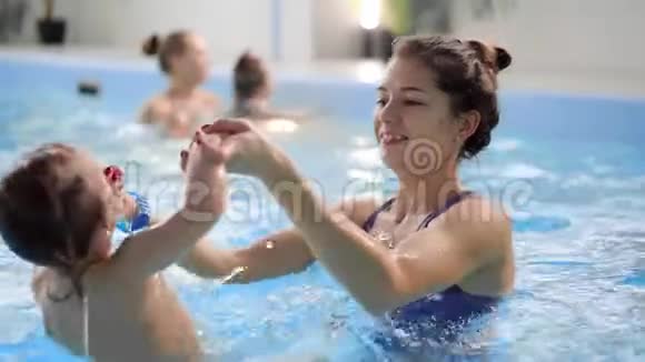 美丽的妈妈教可爱的宝贝女孩如何在游泳池里游泳孩子和妈妈在水里玩视频的预览图