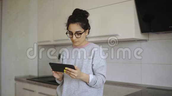 年轻女子在厨房的平板电脑里读东西视频的预览图