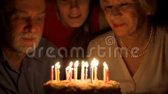 爱的老夫妇和他们的女儿在家里用蛋糕庆祝拥抱和吹蜡烛视频的预览图