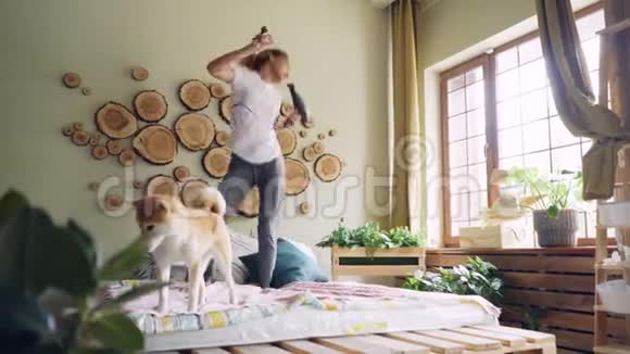 快乐的女学生在床上跳舞在吹风机里唱歌在听音乐时玩得很开心而它的聪明的狗是视频的预览图