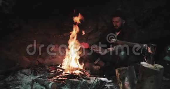 胡须男在篝火上方暖手晚上的晚上游客晚上篝火在大火中抢劫木材视频的预览图