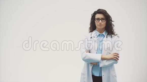 美丽的年轻黑发医生穿着医疗制服在孤立的灰色背景在这段时间里她的听音器视频的预览图