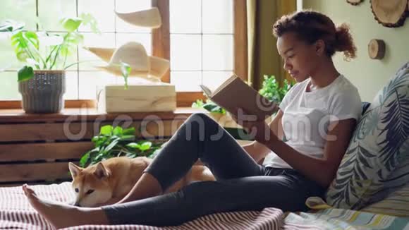 漂亮女孩混血学生正在看书爱抚宠物狗在床上表达爱和关怀视频的预览图