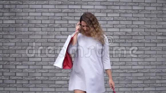 一个购物后带着包裹的女孩心情很好靠在石头墙上慢动作高清高清视频的预览图