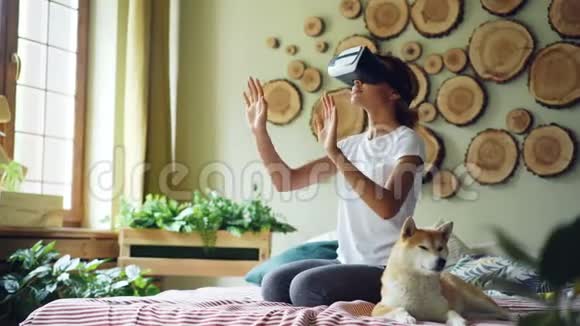 非裔美国女孩在家里用虚拟现实眼镜坐在床上她的手和头在动微笑着视频的预览图