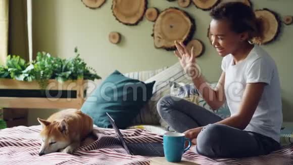 快乐的女孩在网上和朋友聊天打手势看着坐在家里床上的笔记本电脑屏幕视频的预览图