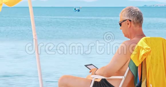 成熟男人在海滩上阅读电子阅读器视频的预览图