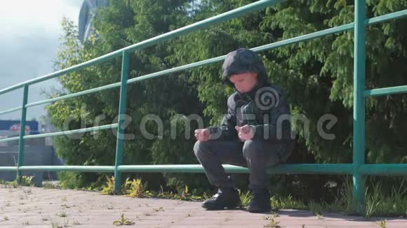 七岁的男孩坐在公园的篱笆上环顾四周视频的预览图
