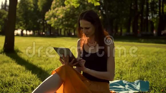 年轻女士在公园里浏览她的平板电脑视频的预览图