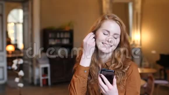 年轻的红发白种人女人听音乐在电话和舞蹈在咖啡馆视频的预览图