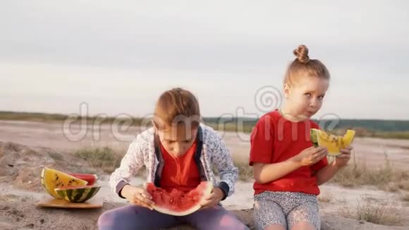 两个女孩在日落时吃西瓜有黄色果肉的西瓜视频的预览图