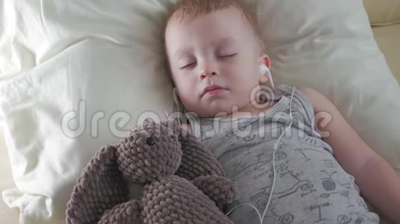 戴着耳机的可爱小男孩和泰迪熊睡在一起视频的预览图