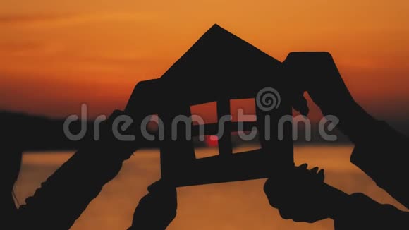 剪影一个用纸板做的小纸屋在海上日落时用手握住效率及家居概念视频的预览图