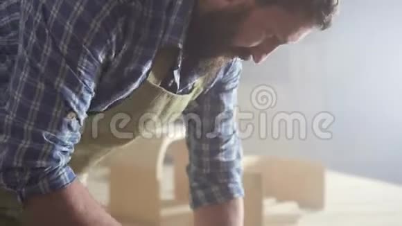 一个穿着衬衫留着胡子的橱柜制造商在一个黑暗的自动技术车间里视频的预览图