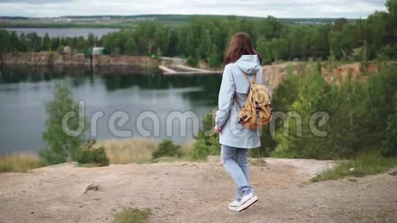 慢镜头描绘年轻的红头发妇女走到悬崖边观看令人兴奋的湖泊森林和风景视频的预览图