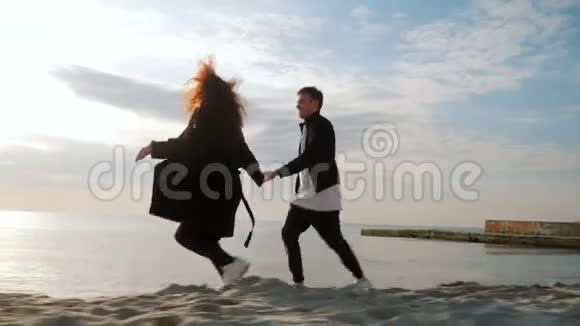 年轻夫妇在沙滩上奔跑玩得开心愚弄牵手享受瞬间浪漫的日落视频的预览图