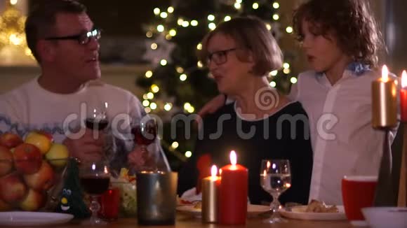 一对年迈的夫妇祖父母和他们的孙子庆祝圣诞节喝红酒祖母亲吻孙子视频的预览图
