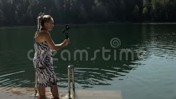女性拍摄手持电影万向节稳定智能手机女孩站在码头自拍博客广播视频的预览图