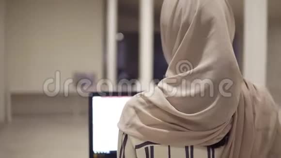 年轻的阿拉伯女性戴着头巾手里拿着她的黑色笔记本电脑走在大厅旁雇员工作视频的预览图