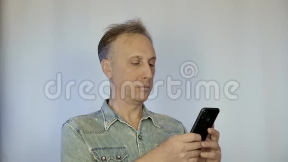 一个中年男人看着智能手机上的照片微笑美好的回忆视频的预览图