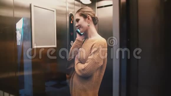 一个年轻放松的欧洲女人坐在透明的玻璃墙电梯上在电话上交谈微笑视频的预览图