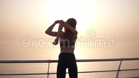 一个瘦长头发的女孩在水边看日出伸展着她的手臂莱金斯和体育视频的预览图