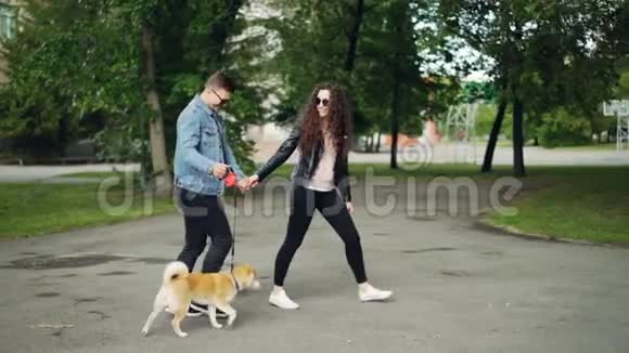 一个年轻漂亮的女人和她的丈夫和可爱的小狗在公园里慢悠悠地散步她在聊天视频的预览图