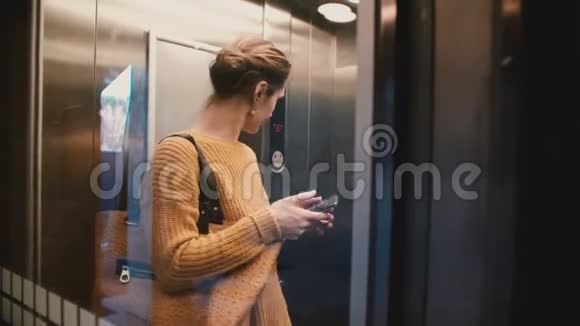 一个有吸引力的压力很大的白人女性乘坐透明的电梯使用智能手机移动办公应用程序视频的预览图