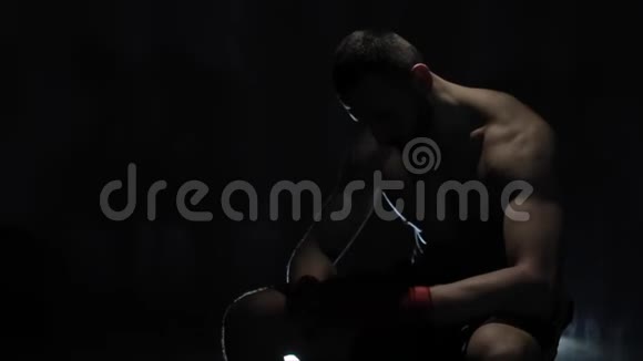 一个肌肉发达的男拳击手坐在黑暗的背景下赤裸上身的强壮运动员视频的预览图