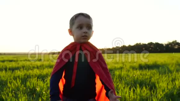 在夕阳的映衬下一个快乐的孩子穿着超级英雄的服装站在绿色的草坪上视频的预览图