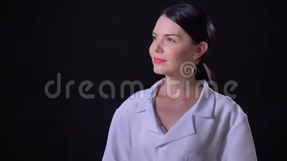 年轻迷人自信的女医生穿着白色外套对着镜头微笑站在黑色背景上视频的预览图