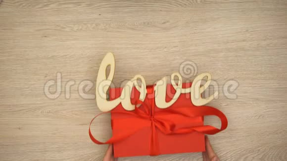 手把带有木制爱词的红色礼盒放在桌上情人节礼物视频的预览图