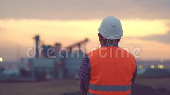 日出时炼油厂的天空背景轮廓和发电厂模糊波克戴着头盔的工程师视频的预览图