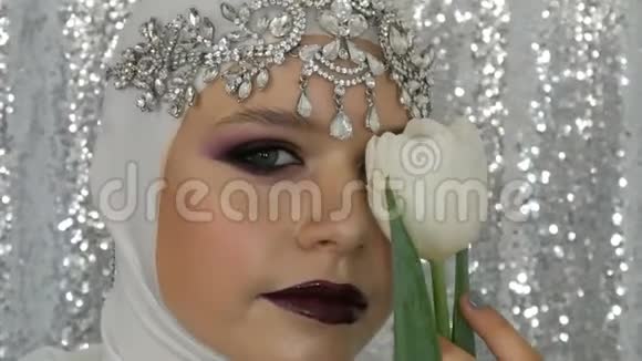 模特和郁金香的脸白色的图像和银色的皇冠有一个明亮的多色化妆叫做烟熏眼摆姿势视频的预览图