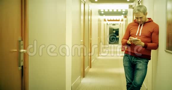 灰发青年穿着休闲装在酒店走廊里使用智能手机视频的预览图