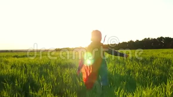 一个穿着超级英雄服装的快乐孩子穿着红色雨衣在夕阳的映衬下沿着绿色的草坪奔跑回首往事视频的预览图