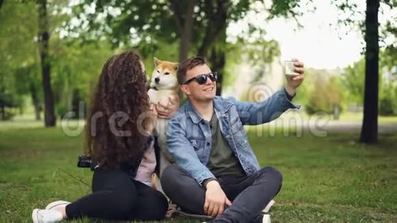 受欢迎的博主正在录制关于他自己的视频他的妻子和可爱的狗男人拿着智能手机说话看着视频的预览图