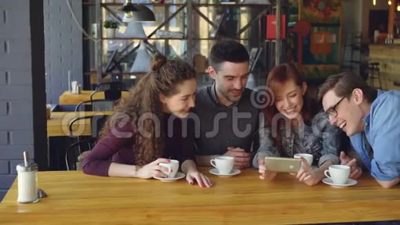 漂亮的朋友们正在观看有趣的视频并在舒适的咖啡馆里喝茶的时候讨论它现代视频的预览图