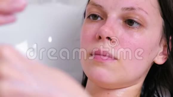 女人把面具戴在浴室里的脸上面的特写白色背景视频的预览图