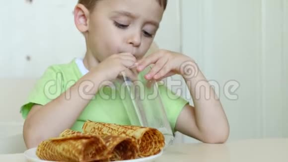 一个快乐的孩子通过吸管喝牛奶吃华夫饼管道坐在桌子旁照相机的移动视频的预览图