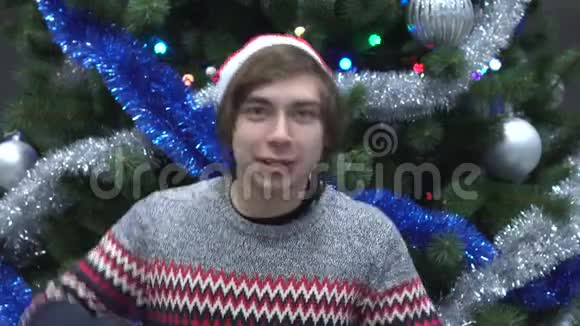 英俊的年轻人戴着圣诞帽在圣诞树背景上跳舞视频的预览图