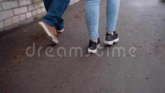一个男人和一个女孩在雨后的潮湿沥青上行走他们的脚在人行道上走着视频的预览图