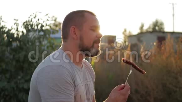 英俊快乐的男人在户外烧烤时吃烤香肠视频的预览图