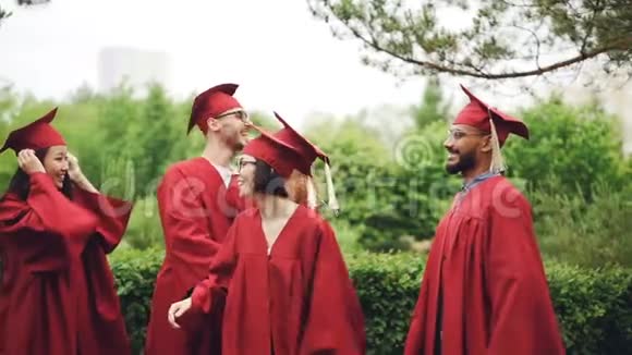 欢快的女孩和即将毕业的学生带着帽子和长袍拥抱和握手的缓慢动作视频的预览图
