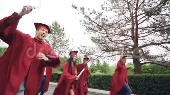 带着毕业证书带着挥舞着卷轴和长袍带着快乐和情绪化奔跑的年轻人的慢动作视频的预览图