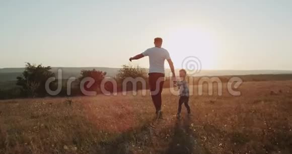 带着三岁的儿子在夕阳下奔跑着年轻的爸爸景色迷人视频的预览图