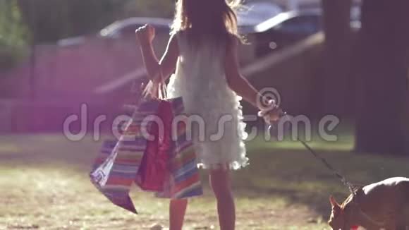 购物者的生活方式时尚的孩子牵着狗在逛完商店后带着很多包在草坪上散步视频的预览图