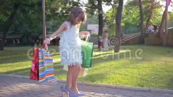 孩子们在购物穿着高跟鞋的时髦小女孩手里拿着很多纸袋走路视频的预览图