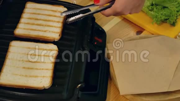 在厨房做三明治用钳子的手俯视图从三明治制造者手中取出烤好的白吐司面包视频的预览图