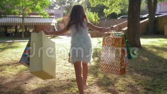 季节性的销售买了很多东西的小女孩正在阳光下沿着草坪奔跑视频的预览图